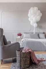 Birthday decoration in grey stylish bedroom with comfortable bed, trendy armchair and basket with...