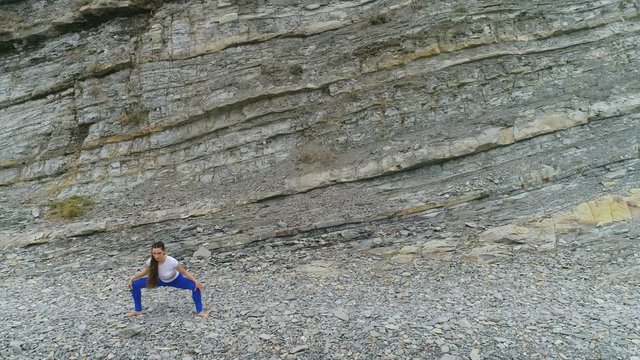 Woman is doing plie squats the bodyflex on the rock and sea background. Aerial beautiful footage view.