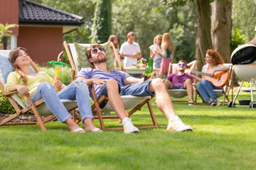 Man and woman relaxing on sunbeds during grill party with friends in the garden