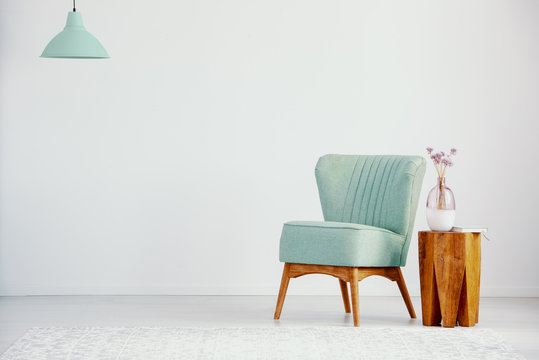 Green armchair next to wooden table with plant in loft interior with copy space and lamp. Real photo