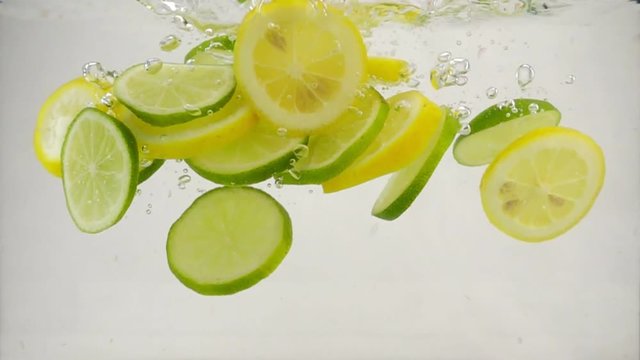 Slices of citrus lime and lemon fall into the water with splashes and bubbles, slow motion close-up
