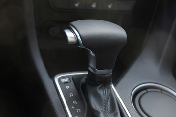Car interior. Black leather automatic gearbox with chrome button and round ashtray with sunlights and bokeh on front