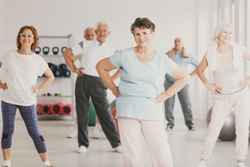 Smiling elderly woman holding hips during gymnastic classes for senior people