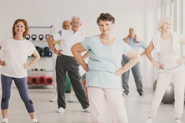 Poster Smiling elderly woman holding hips during gymnastic classes for senior people © Photographee.eu
