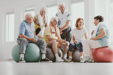 Low angle on smiling senior people on balls after gymnastic classes at sport club