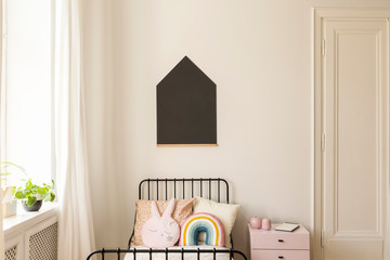 Black poster on white wall above child's bed in bedroom interior with pink cabinet and door. Real...