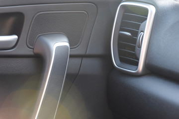 Car inside. Black plastic automobile door with chrome elements, buttons and air grid, part of door handle with blurred colorful bokeh on front