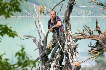 A man stands on a fallen tree in the water. A tourist stood on the trunk of a tree fallen from the wind in a mountain lake.