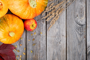 Autumn harvest Thanksgiving pumpkins, apples, wheat ears and fallen leaves on wooden background. Seasonal Fall Food