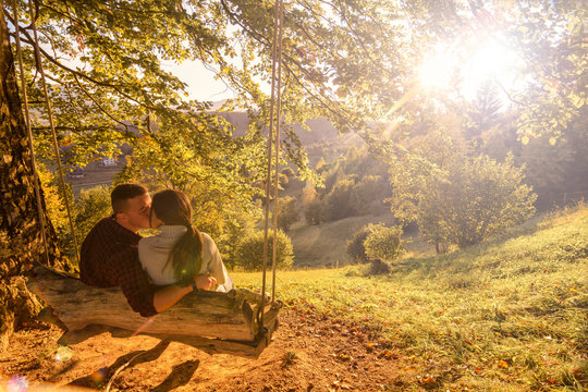 Couple in love (boy and girl) ride on a swing in nature and kiss. With lights effects.