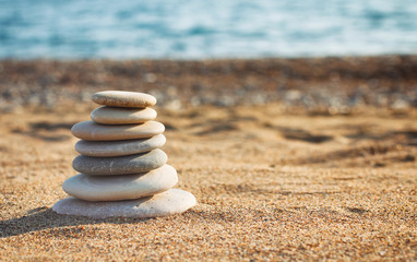 Zen pyramid of spa stones on the blurred sea background. Sand on a beach. Sea shores. Water waves texture. Left side of photo. Place for text. 