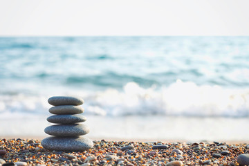 Zen pyramid of spa stones on the blurred sea background. Sand on a beach. Sea shores. Water waves texture. Left side of photo. Place for text. 