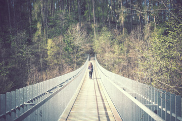 lonely young woman crosses a bridge vintage effect, she is walking in a forest