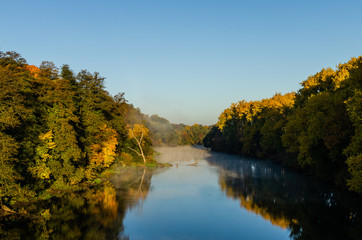 Autumn sunrise on the river with fog. The fog spreads in the morning along the river with tall trees on the shore.
