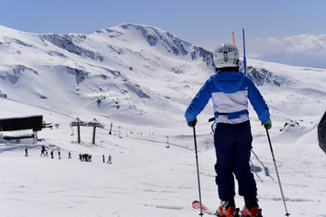 A boy in a blue  ski jumpsuit skiing from the snowy mountains of the Sierra Nevada