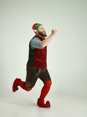 The happy smiling friendly man dressed like a funny gnome or elf running on an isolated gray studio...