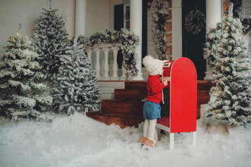 A little baby girl in a white knitted hat makes a wish and writes a letter to Santa Claus and sends...