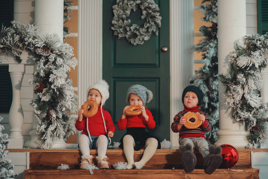 Children sitting on the porch of their house together, Eat bagels. Merry Christmas, happy New Year. Yard with a christmas tree, lights and decorations. Miracle time.