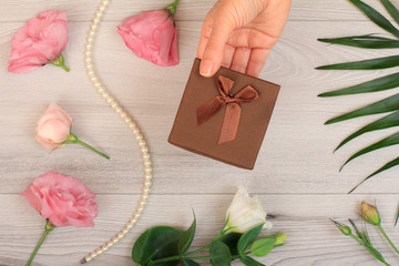 Wooman holding a gift box tied in the hands with flowers on the background.