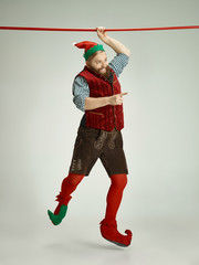 The happy smiling friendly man dressed like a funny gnome or elf hanging on an isolated gray studio...