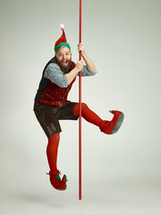 The happy smiling friendly man dressed like a funny gnome or elf posing on an isolated gray studio...