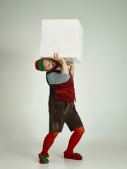 The happy smiling friendly man dressed like a funny gnome or elf posing on an isolated gray studio...