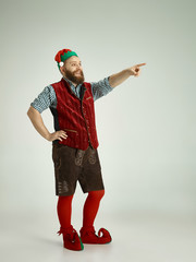 The happy smiling friendly man dressed like a funny gnome or elf pointing to left on an isolated gray studio background. The winter, holiday, christmas concept