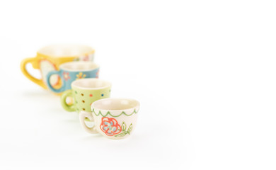 Four teacups in a row on white background. Shallow depth of field with focus on closest cup. Varying colours, patterns and sizes in ascending order. Pretty bright pastel colours. With copy space.