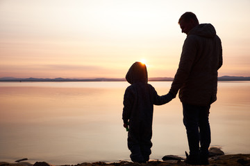 Fototapeta premium Father and little son silhouettes at sunset outdoor. Lifestyles concept.