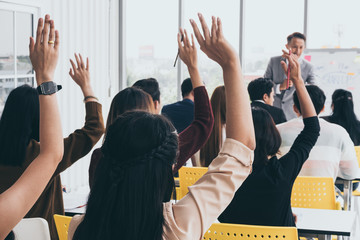 Audience raising hands up while businessman is speaking in training at the office.