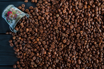 Fototapeta premium Roasted fragrant grains of black coffee are scattered from a white metal bucket on a black table