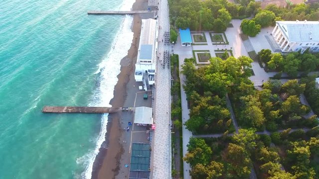 Aerial view Drone fly alley along beach, small storm is not expected cloudy, pier to Black Sea. Waterfront Stretches Across Coastline Resort Town cityscape Sudak of town, Crimea.