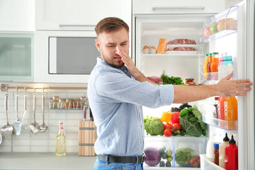 Man feeling bad smell from stale products in refrigerator at home - obrazy, fototapety, plakaty