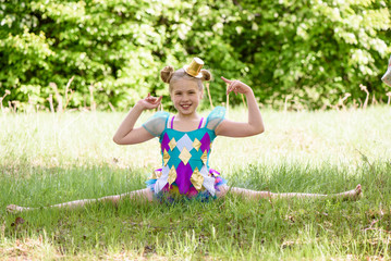 Young sporty blond girl sitting on grass in the park,gymnastic splits