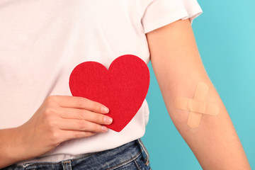 Woman holding heart near hand with adhesive plasters against color background, closeup. Blood...