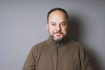 Fototapeta premium middle aged man in his 40s with short dark hair and graying beard smiling against gray wall with copy space