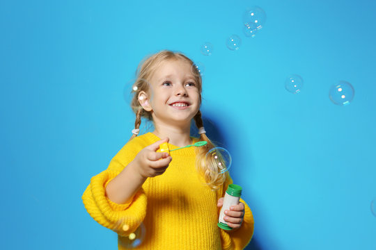 Cute little girl blowing soap bubbles on color background. Space for text