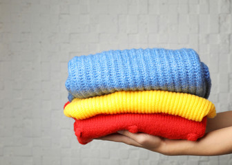 Woman holding stack of folded warm knitted sweaters against brick wall