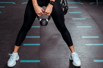 Partial view of sportive girl squatting with kettlebell in sports gym