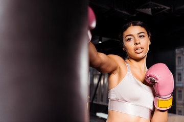 Fototapeta na wymiar Attractive strong girl in pink boxing gloves practicing boxing in gym