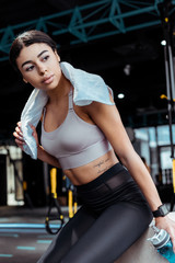 Fototapeta na wymiar Attractive sportive girl with towel and sport bottle looking away in fitness gym