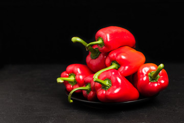 Red peppers in plate on black background - closeup photo of whole fresh ripe sweet vegetables in dark mood style.