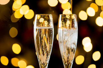 Background of two glasses of champagne, spruce branches on red table cloth. Living room decorated with lights and candles and Christmas tree
