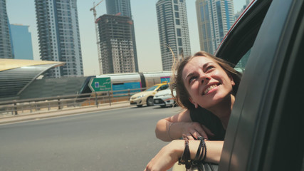 A happy girl sits on the back seat of a car and travels around the city of Dubai.