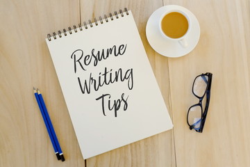 Top view of pencil,glasses,a cup of coffee and notebook written with Resume Writing Tips on wooden...