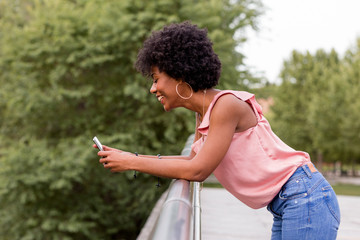 Happy young beautiful afro american woman smiling and using mobile phone. Green background. Spring or summer season. Casual clothing outdoors