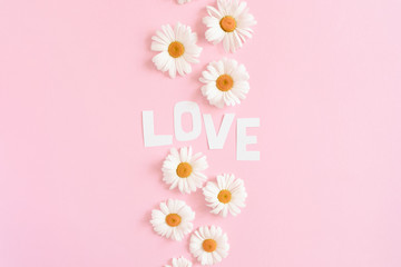Word Love made of letters cut out of paper. Pattern made of white chamomile on a pink pastel background