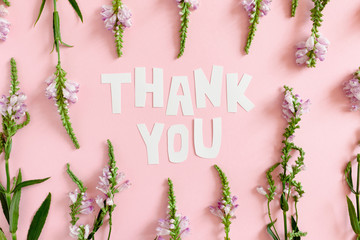Quote Thank You made of letters cut out of paper. Pattern made of wild flowers on a pink pastel...
