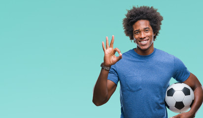 Afro american man holding football ball over isolated background doing ok sign with fingers,...