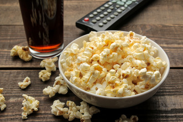 Popcorn, coca cola and TV remote on a brown wooden background. concept of watching movies at home.